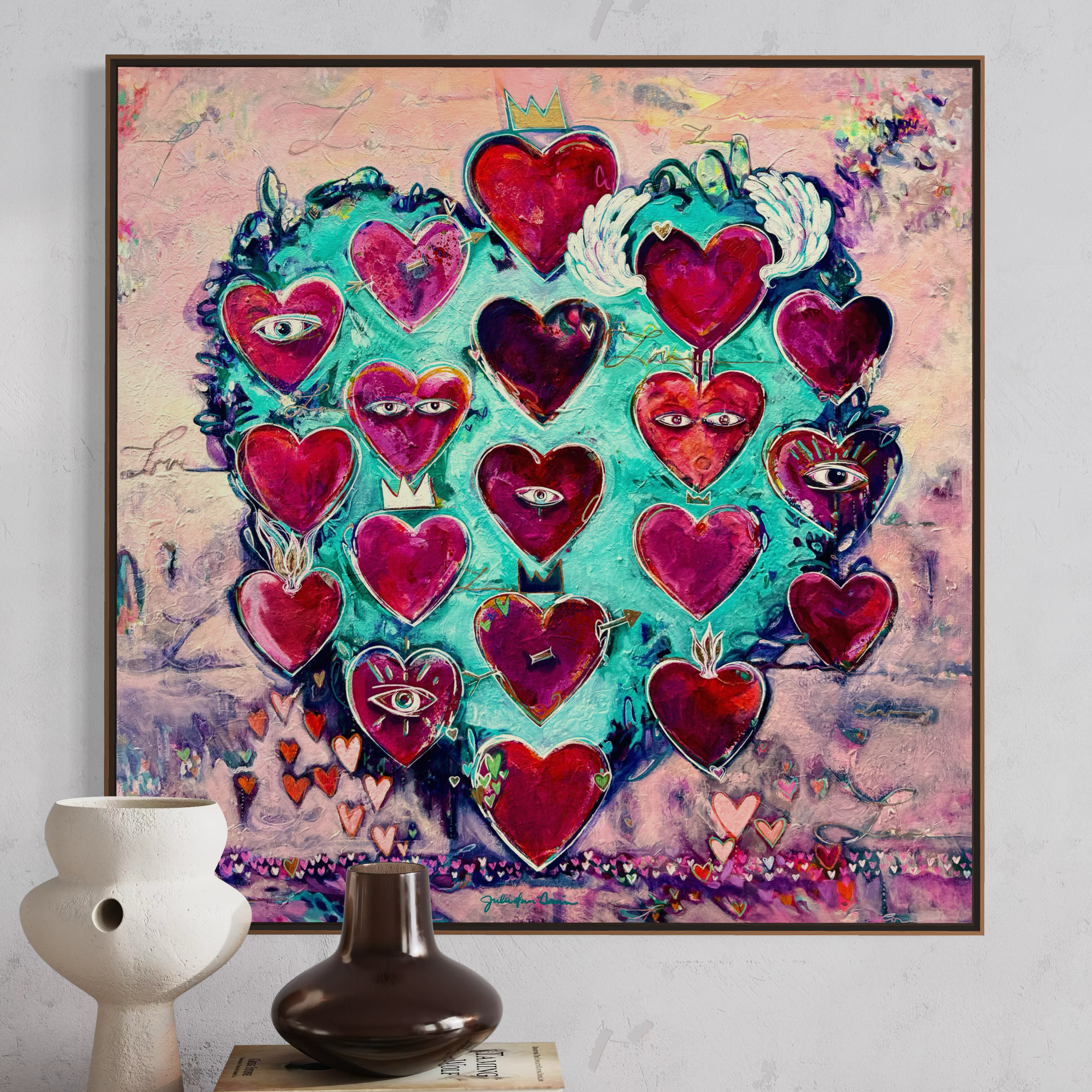 Love Always Wins Artwork by Julie Davis. Framed artwork with colorful hearts on a wall above a table with decorative items.