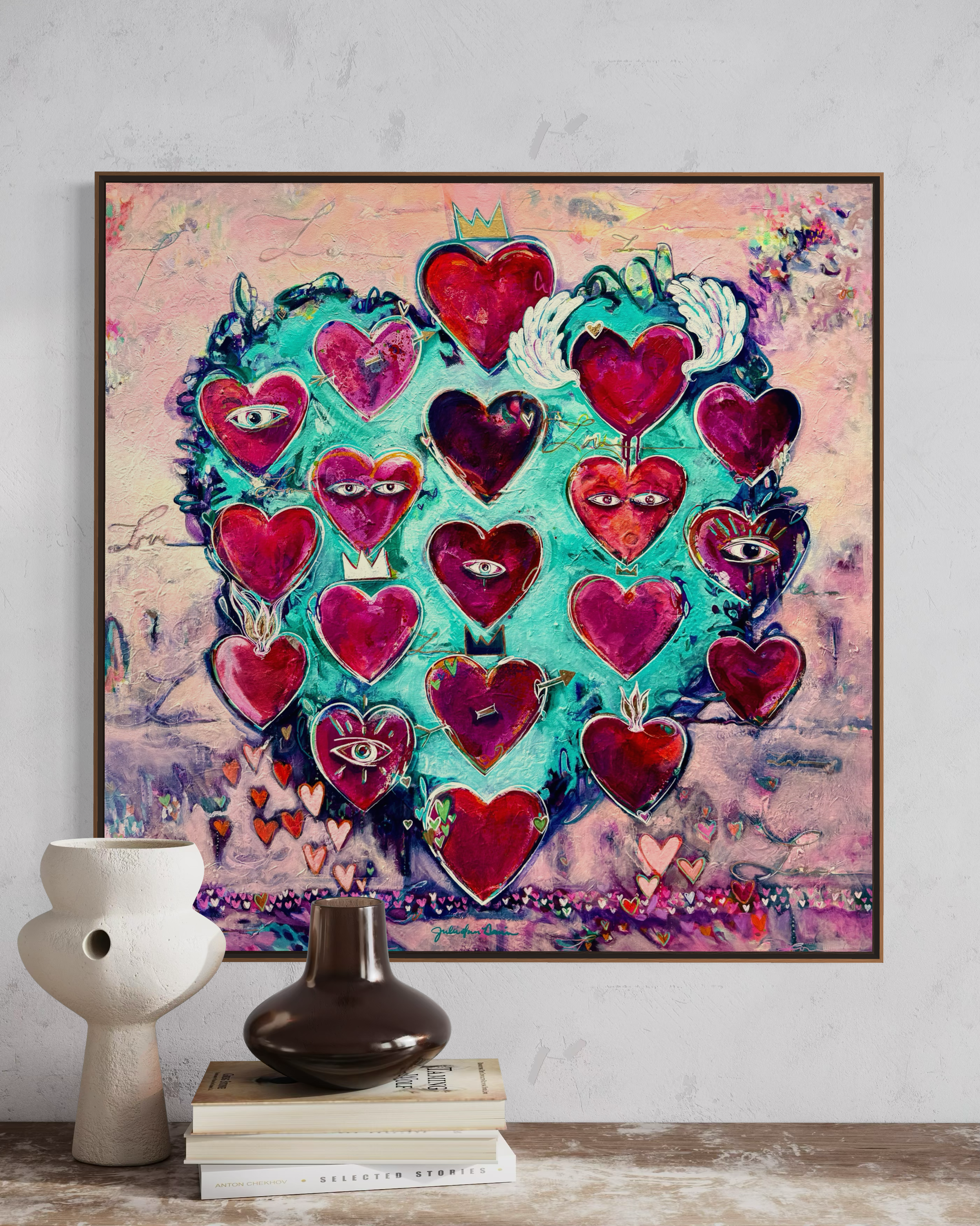 Love Always Wins Artwork by Julie Davis. Framed artwork with colorful hearts on a wall above a table with decorative items.